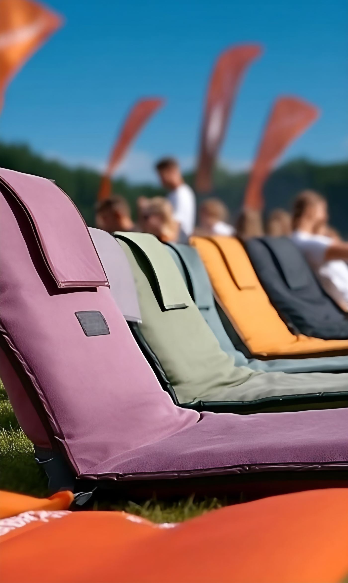 Rij Festiseat grondstoelen in oudroze, lila, salie, grijsblauw, oranje en antraciet op een festivalveld